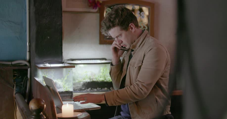 A man talks on the phone while typing on his laptop