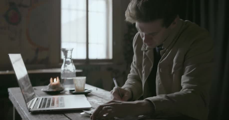 A man is working using a laptop and taking notes