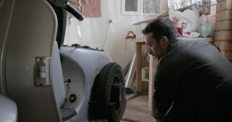 A man works on a scooter in a garage