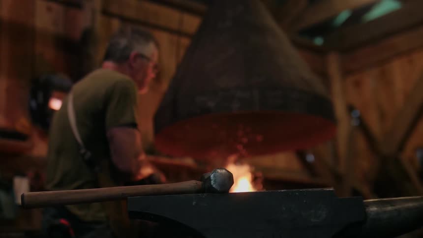 A blacksmith is working in his shop by the fire