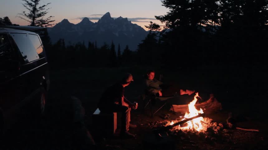 Campers gather around a campfire at dusk