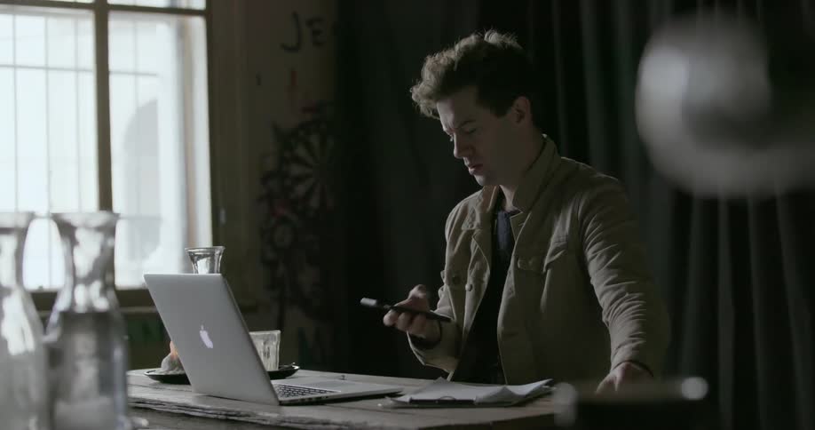 A man talks on a phone and works on a laptop