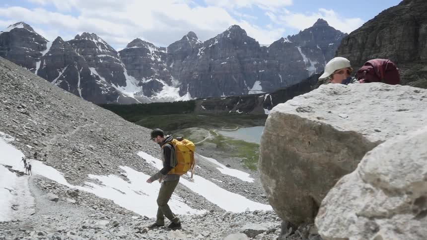 Two people surrounded by mountains wear hiking gear as they walk