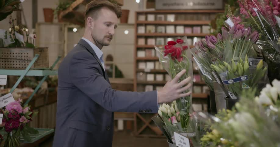 A man selects a bouquet of red flowers from a florist shop