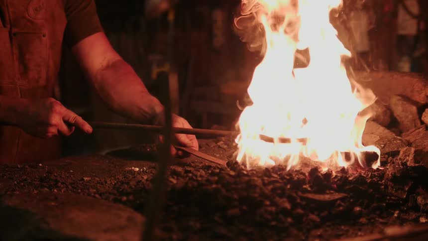 A blacksmith stirs the fire with a poker