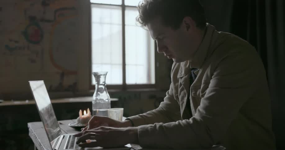 A man takes a drink and types on a laptop