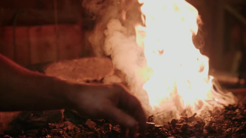 A man is throwing some coal pieces in the fire