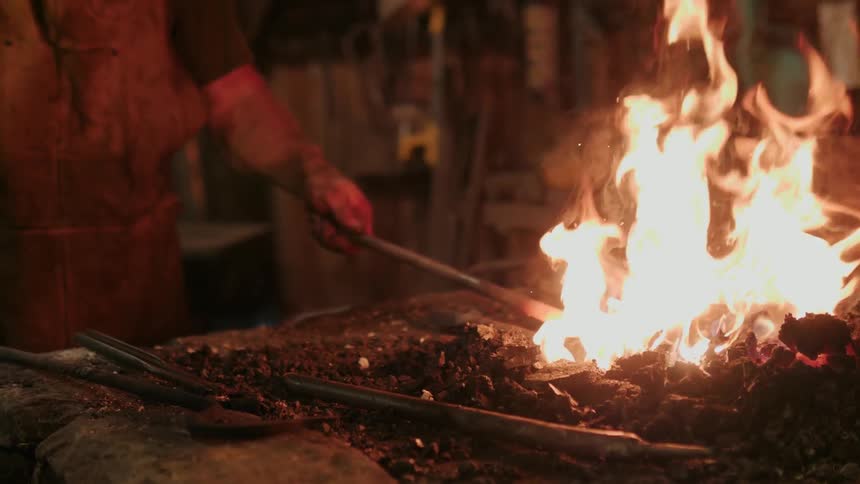 A blacksmith lifts a hot iron from the flame