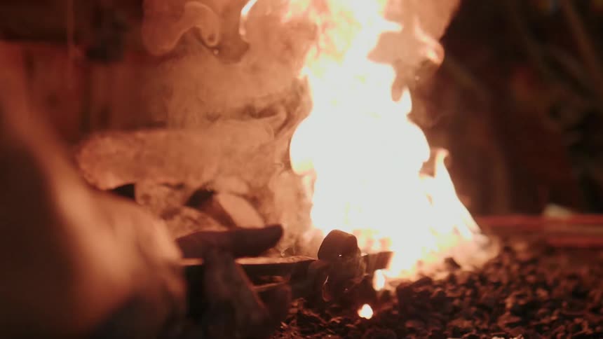 A blacksmith heats a piece of metal in a fire