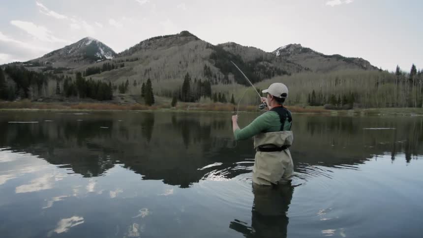 Woman is fly fishing in a lake in the mountains