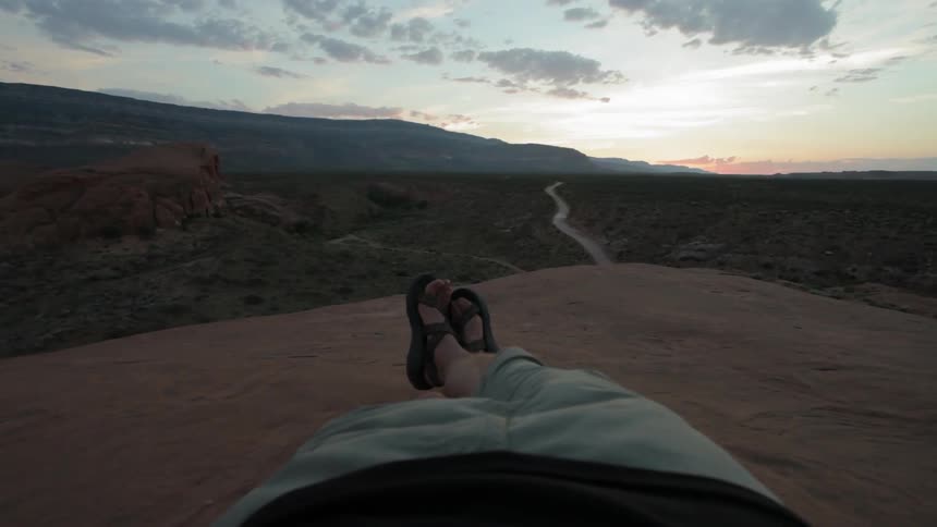 A man lays on a large rock in the wilderness at sunset