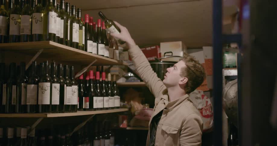 A man inspects a stock of wine bottles in a closet