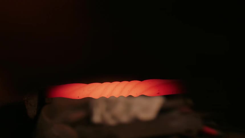 A person is forming some hot metal on an anvil