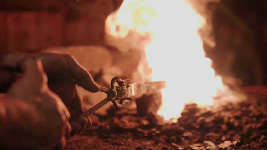 A blacksmith turns the metal in the flame