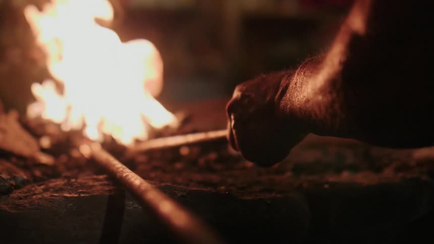 A person moves a poker into the flame