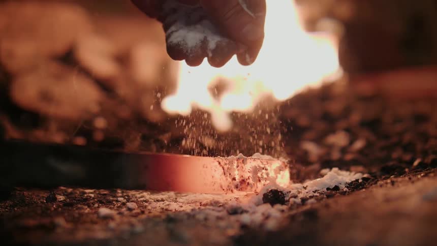 Iron worker sprinkles flux powder on burning metal