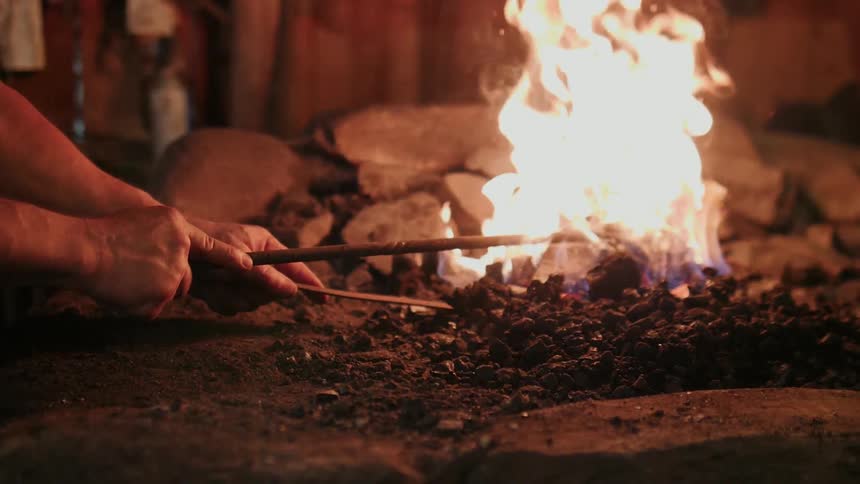 A blacksmith holds tools in a burning fire