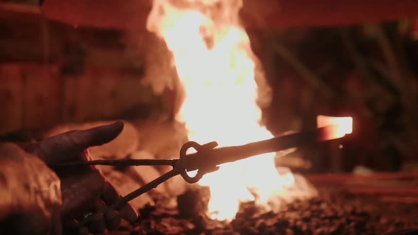 A blacksmith heats a piece of metal in a fire