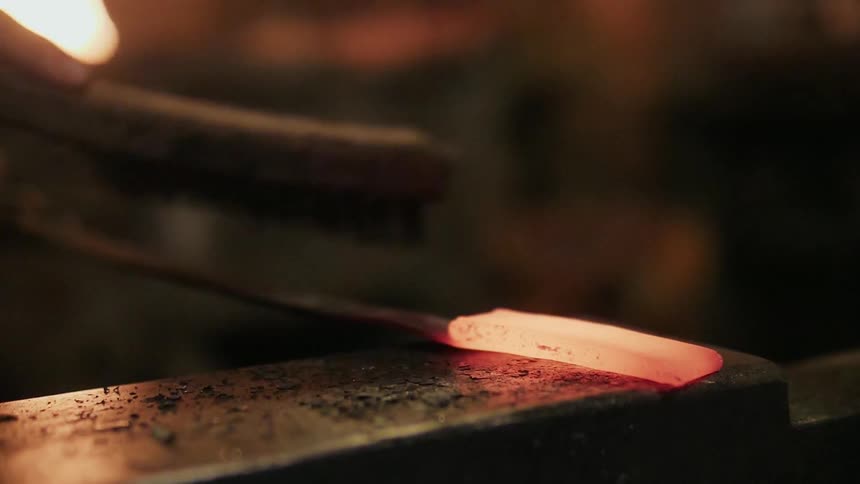 A blacksmith uses a wire brush on heated metal