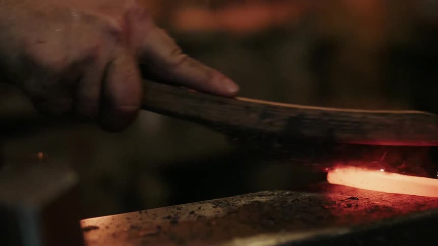 A blacksmith rubs a wire brush on a piece of hot metal