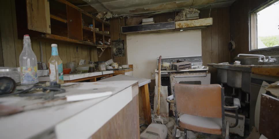 The  interior of a house that is falling apart is littered with trash