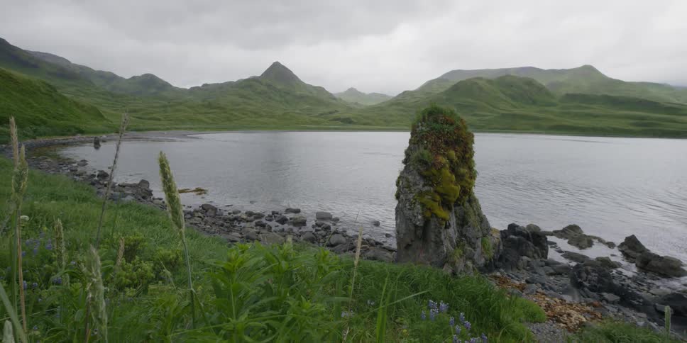 A lake laps a grassy shoreline in a mountain scene on a cloudy day