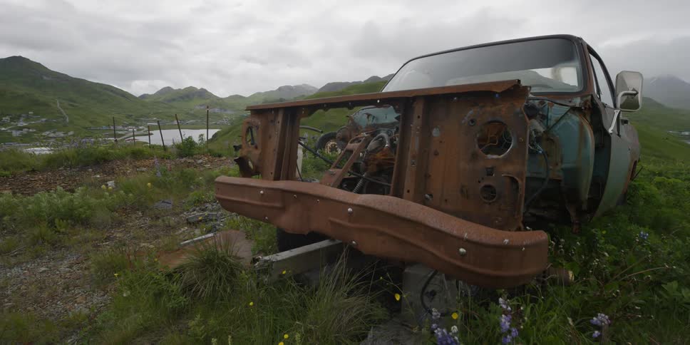 Rusted out car sits on a grassy hill near the water