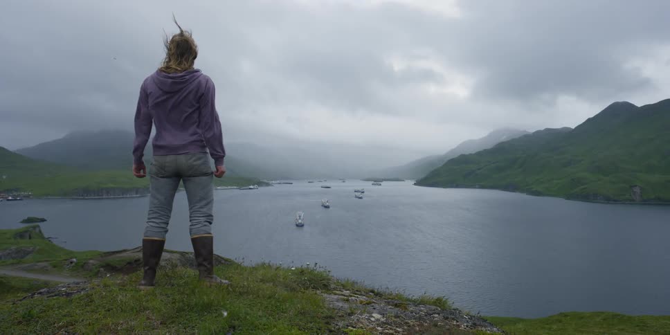 Man stands on a hill overlooking a bay as the windy blows