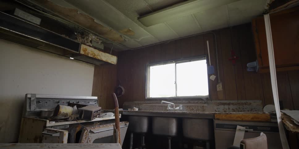 Rusty appliances sit in an abandoned kitchen