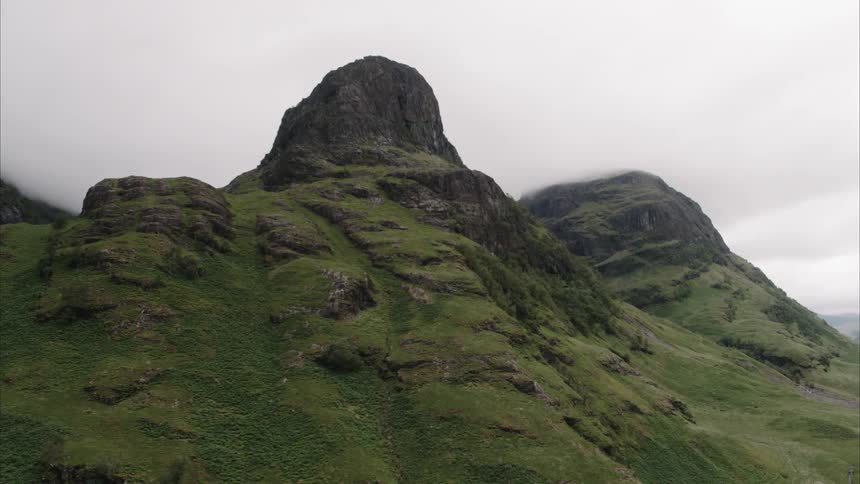 A rocky cliff on top of a lush green hill