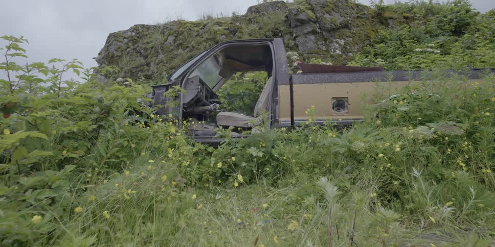 A car is wrecked and abandoned up on a hill