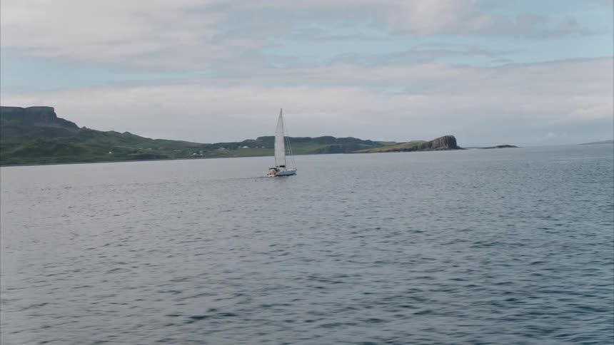 A sailboat moves across the ocean near a coastline during the day