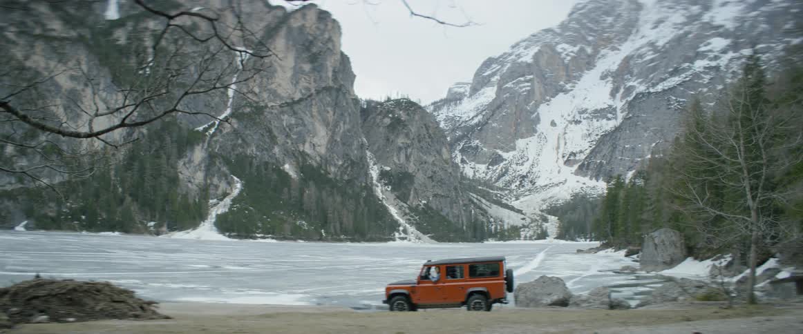Person driving slowly near frozen lake and snowy mountains
