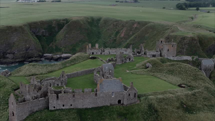Castle ruins on top of a green hill next to the ocean