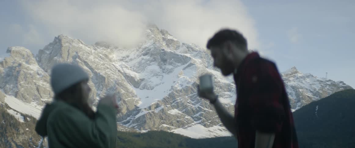 A man and woman drink from mugs in snowy mountains