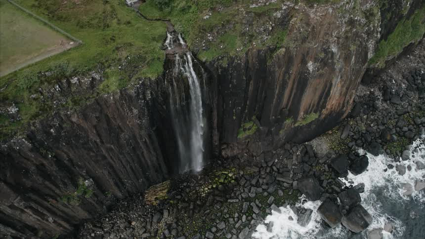 A waterfall flows over a coastal cliff