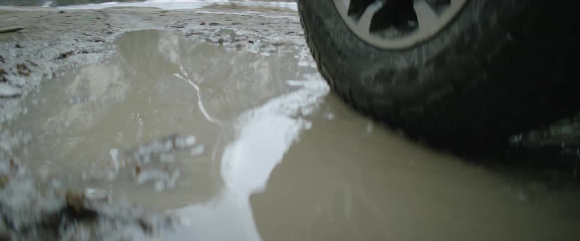 A car tire rolls through a muddy puddle