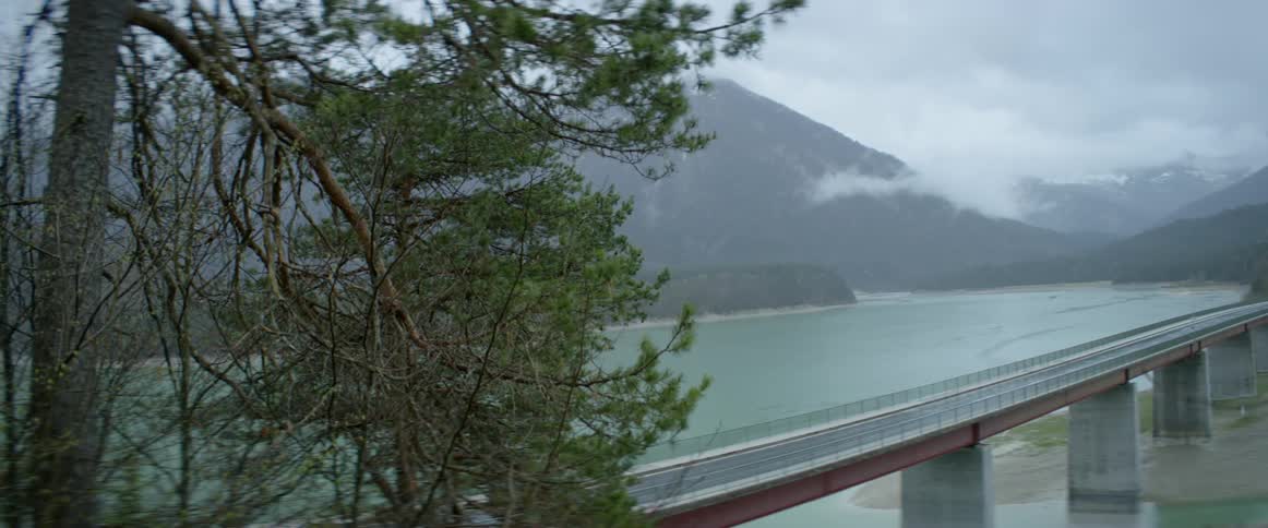 A vehicle drives on a bridge next to a mountain lake