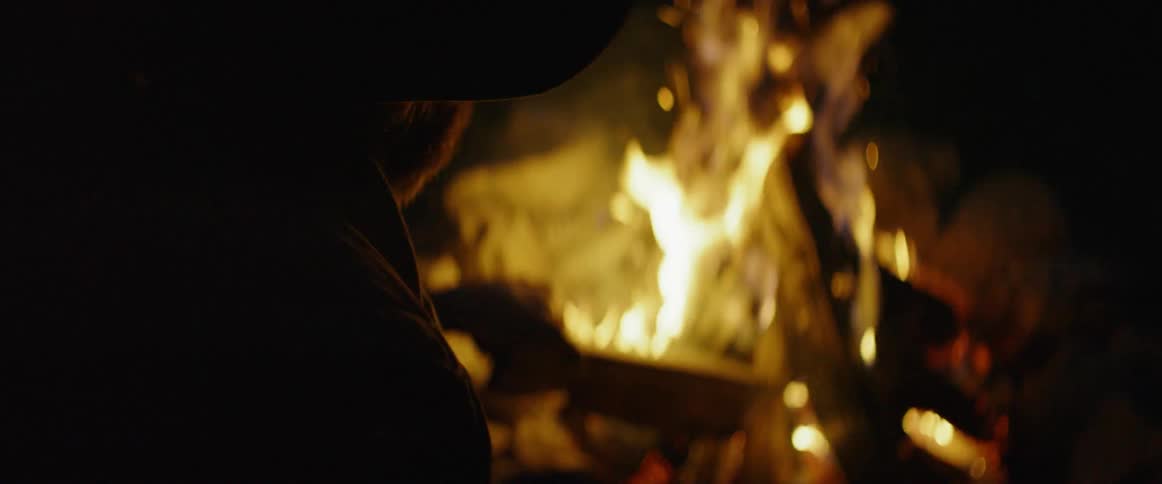 A man sits next to a campfire