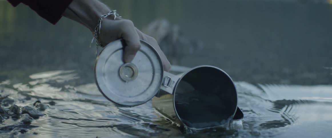 A woman scoops up lake water into a kettle