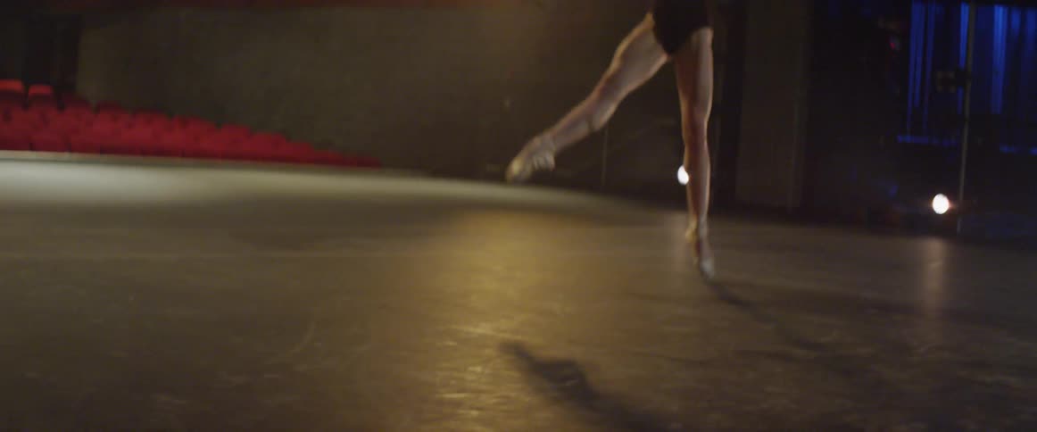 Young ballerina is leaping and dancing on stage in auditorium