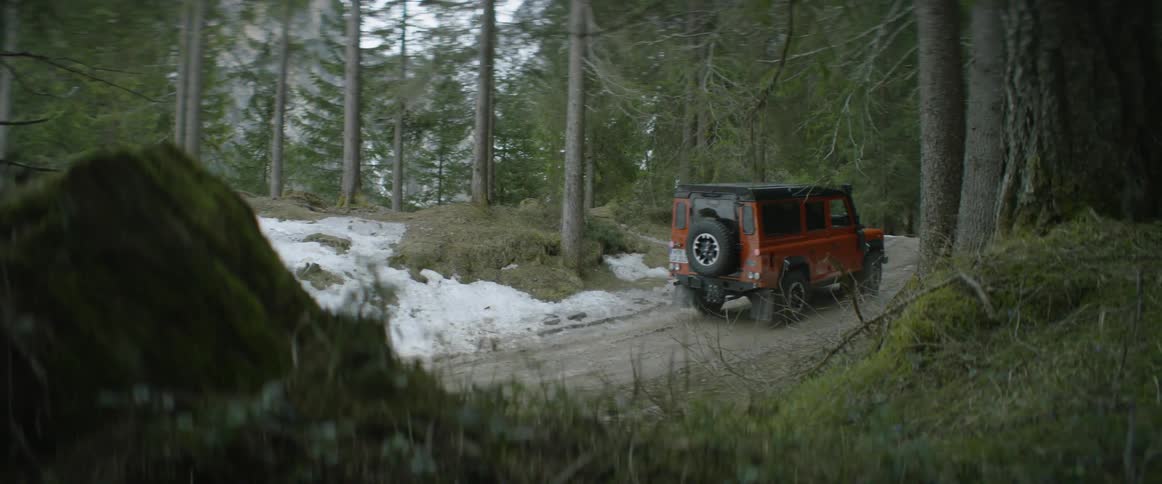An suv is driving on a narrow road through a forest in winter