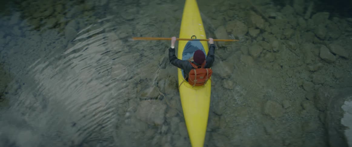 A person paddles a kayak across clear water