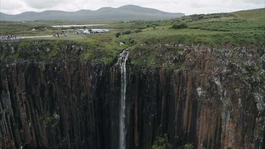 Water falls off the edge of a steep cliff as people look on