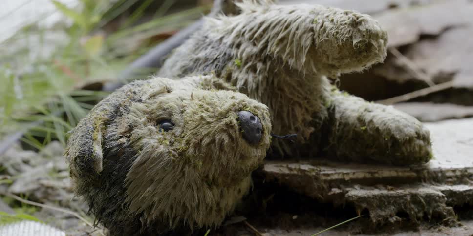 A stuffed toy animal lies discarded on a pile of mud and trash during the day