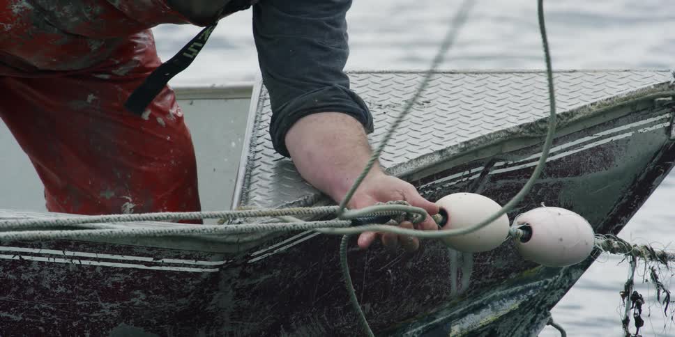 Man on a boat ties some rope to net