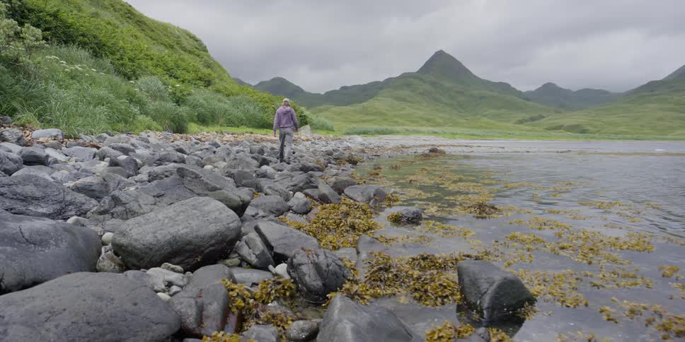Man walks across rocks beside the shore
