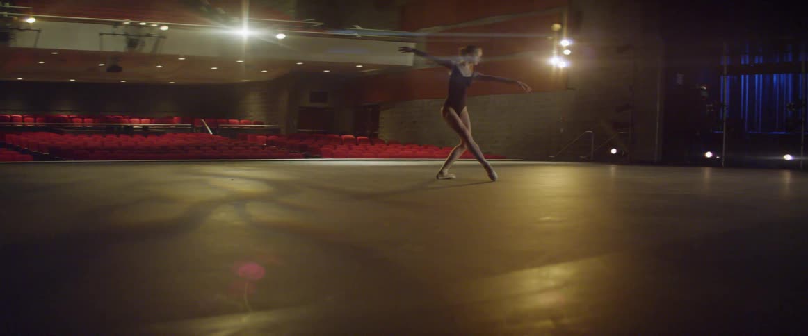 Young ballerina is dancing on stage in auditorium