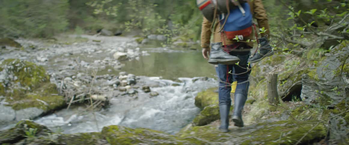 Three people are hiking along a stream in the woods