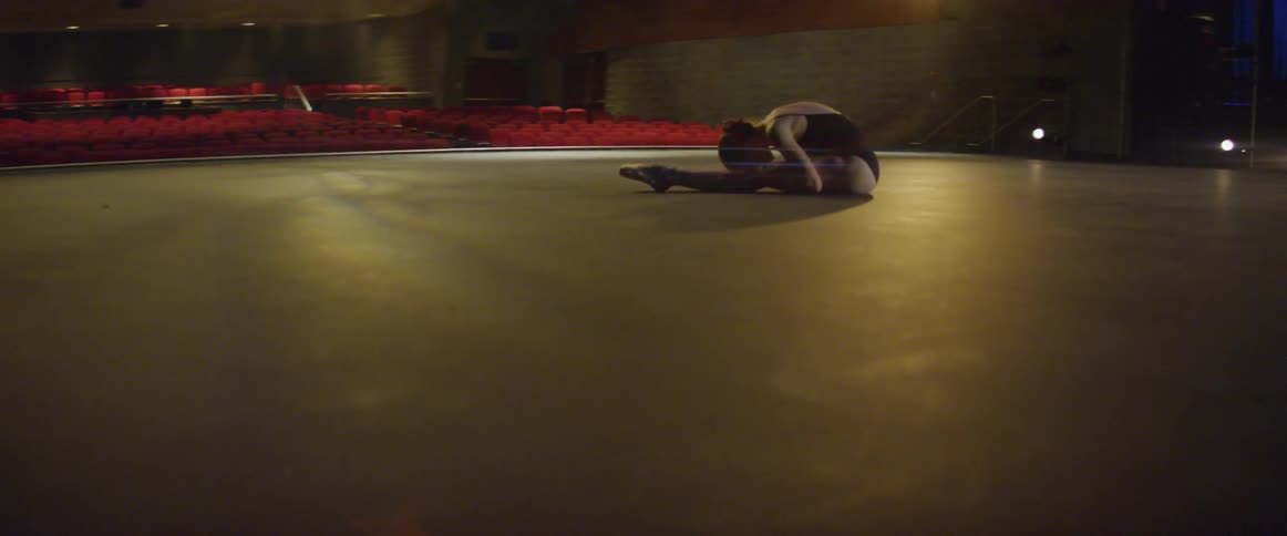 Woman stretches in the middle of an auditorium stage